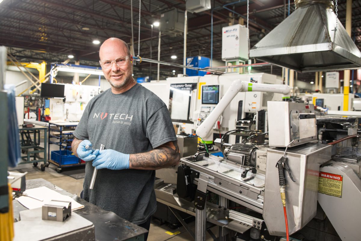Vérification des mesures d'une pièce usinée par un employé devant une machine CNC